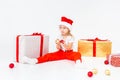 Little blonde kids in Santas hat sitting between gift boxes and playing with christmas balls. Isolated on white background. Royalty Free Stock Photo