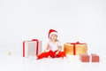 Little blonde kids in Santas hat sitting between gift boxes and playing with christmas balls. Isolated on white background. Royalty Free Stock Photo