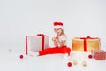 Little blonde kids in Santas hat sitting between gift boxes and playing with christmas balls. Isolated on white Royalty Free Stock Photo