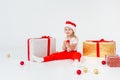 Little blonde kids in Santas hat sitting between gift boxes and playing with christmas balls. Isolated on white Royalty Free Stock Photo