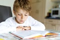 Little blonde school kid boy reading a book at home