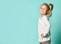 Little blonde schoolgirl with ponytail, in shirt with hearts print. Smiling, hands on hips, posing on blue background. Close up Royalty Free Stock Photo