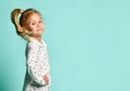 Little blonde schoolgirl with ponytail, in shirt with hearts print. Smiling, hands on hips, posing on blue background. Close up Royalty Free Stock Photo