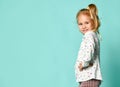 Little blonde schoolgirl with ponytail, in shirt with hearts print. Smiling, hands on hips, posing on blue background. Close up Royalty Free Stock Photo