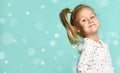 Little blonde schoolgirl with ponytail, in shirt with hearts print. Smiling, hands on hips, posing on blue background. Close up Royalty Free Stock Photo