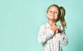 Little blonde schoolgirl with ponytail, in shirt with hearts print. Smiling, posing on blue background. Close up Royalty Free Stock Photo