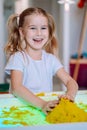 Little blonde smiling girl play with yellow magic sand on white glowing table. Sensory development. Lessons in