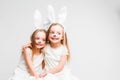 Little blonde twins in white dresses with rabbit ears. Studio photo on gray background. Kids celebrate Easter.