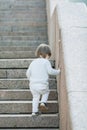 Little blue-eyed boy with long hair climbs the stone stairs. The concept of growing up