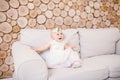 Little blue-eyed girl blond in a white tulle dress with a decoration on her head playing and rejoicing on a beige sofa in a room w Royalty Free Stock Photo