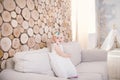 Little blue-eyed girl blond in a white tulle dress with a decoration on her head playing and rejoicing on a beige sofa in a room w Royalty Free Stock Photo