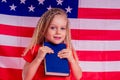 Little Blue eyes blonde charming girl holding an encyclopedia book alphabet foreign language against american flag Royalty Free Stock Photo