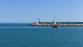 A little boat is sailing in front of the pier of Pesaro harbor with breakwaters and a small red lighthouse Italy, Europe Royalty Free Stock Photo