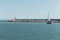 A little boat is sailing in front of the pier of Pesaro harbor with breakwaters and a small red lighthouse Italy, Europe Royalty Free Stock Photo