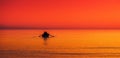 little boat in a sea water, red orange sky at sunset