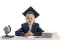 Little bored boy is balancing pencil on his nose while doing homework. Schoolboy in students hat at the table next to notebooks Royalty Free Stock Photo