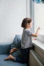 Little bored brunette girl sitting at home and looking at the window