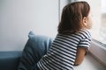 Little bored girl child sitting at home and looking at the window