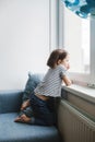 Little bored girl sitting on the couch at home and looking at the window Royalty Free Stock Photo