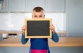 little boy in apron holding chalkboard in kitchen