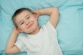 Little boy awakes in his bed and smiles. Toddler in white shirt