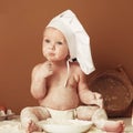 Little boy baker in a chef`s hat sitting on the table playing with flour on a brown background with a wooden rolling pin, a round Royalty Free Stock Photo