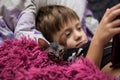 A little boy with a bald cat Sphinx lie in bed under a red blanket and look at the tablet Royalty Free Stock Photo