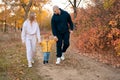 Little boy being holding hands by parents on family autumn walk through countryside. Happy sports family on a walk in Royalty Free Stock Photo