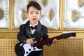 A little boy in black tuxedo stands with guitar Royalty Free Stock Photo