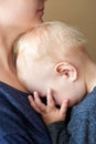 A little boy with blond hair covered his face with hands and sleeps on his mother`s chest Royalty Free Stock Photo