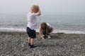 A little boy with blond hair and a girl playing with pebbles on the beach