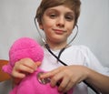 Little boy with blond hair playing with stethoscope at doctor`s office. Pink plush toy in the hands of a child. Doctor game. Boy Royalty Free Stock Photo