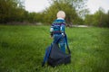 The little boy with blond hair pulling a large backpack chery on the green grass in nature, travel, baby, adventure Royalty Free Stock Photo