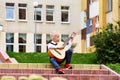 Little boy blond sits on steps in front of school and plays an acoustic guitar.