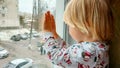 A little boy with blonde hair sits by the window on the windowsill and looks out the window. Winter. New Year& x27;s Royalty Free Stock Photo