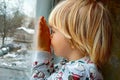 A little boy with blonde hair sits by the window on the windowsill and looks out the window. Winter. New Year& x27;s Royalty Free Stock Photo