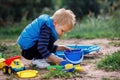 A little boy in blue clothes plays with sand in nature. The child has a beautiful colorful set of plastic beach toys Royalty Free Stock Photo