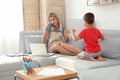 Little boy bothering mother at work in living room. Home office concept