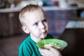 Little boy with bright blue eyes in green t-short eats spaghetti from green bowl