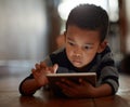 Little boy, browsing and on digital tablet or playing games or streaming video on the internet and lying on the floor at