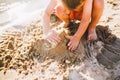 A little boy builds figures from the sand on the shore of the pond at sunset of the day, hands dig up the sand in crisp plan