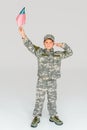 little boy in camouflage clothing saluting while holding american flagpole in hand Royalty Free Stock Photo
