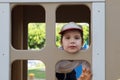 Little boy in cap looks into window in wooden house Royalty Free Stock Photo