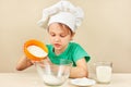 Little boy in chef hat pours flour for baking cake