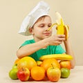 Little boy in chefs hat peeling fresh banana at table with fruits Royalty Free Stock Photo