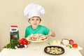 Little boy in chefs hat shows how to cook pizza Royalty Free Stock Photo