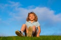 Little boy child with a cute expression face sitting on grass. Cheerful kid having fun on green summer meadow. Royalty Free Stock Photo