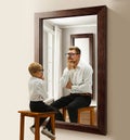 Little boy, child sitting near mirror and imagining him being adult man. Thinking abut future. Conceptual collage. Age
