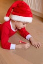 A little boy in Christmas clothes writes a letter to Santa lying on the floor