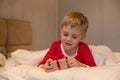A little boy in Christmas pajamas unpacks a gift while lying in bed